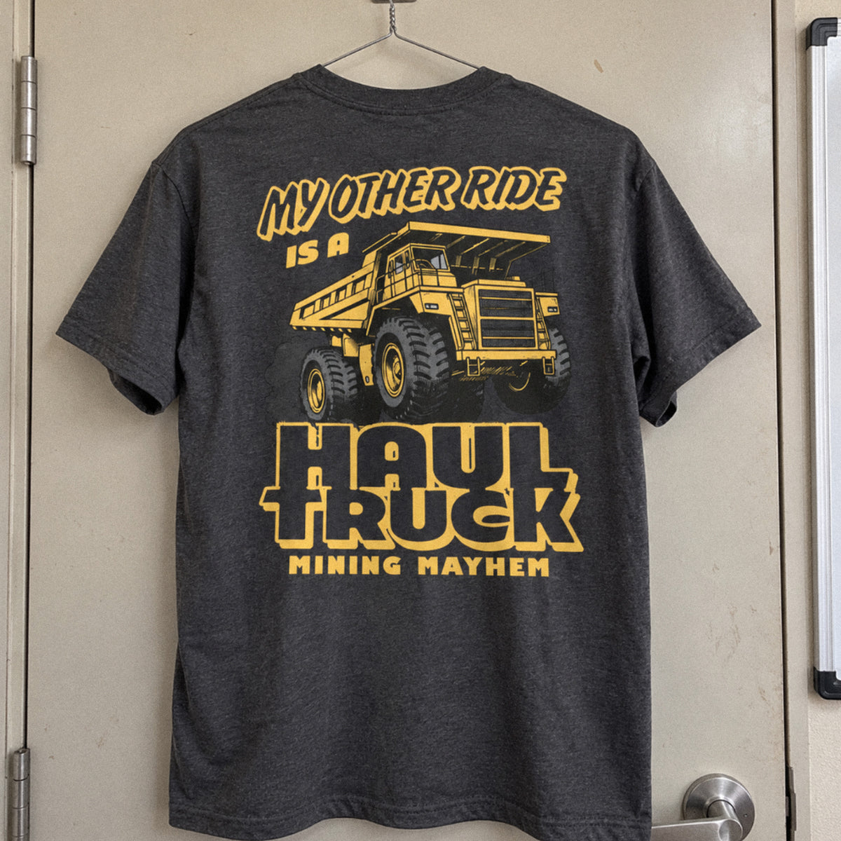 Charcoal Haul Truck t-shirt hanging on a site office door, back print
