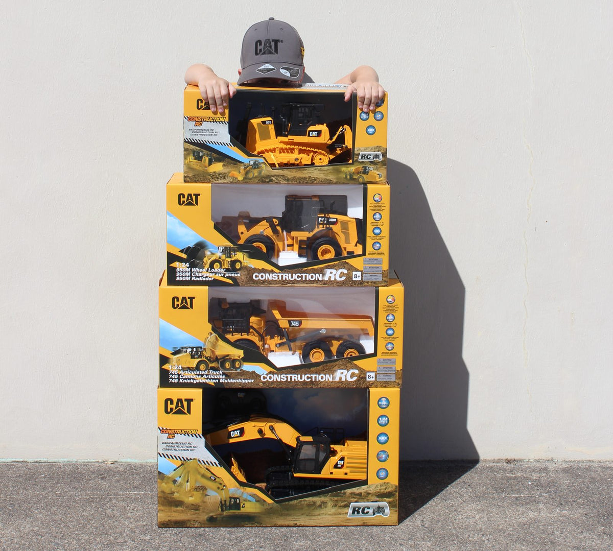 Kid peeking over a stack of four CAT RC machine boxes